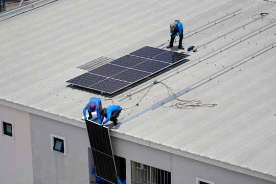 Technicians in blue uniforms collaborate to secure and lift heavy solar modules onto a metallic frame on a building roof for sustainable power