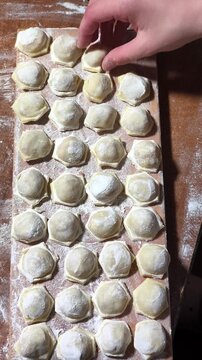 Placing freshly made raw dumplings onto a floured wooden board in a row