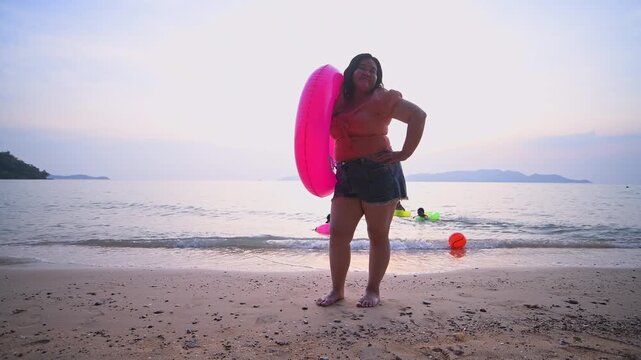 Woman chubby along the shoreline with enjoying bright smile carrying inflatable swim ring perfect for simple pleasure of enjoying nature and leisure vacation time by the sea.	