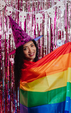 Young woman wearing a witch's hat and holding an LGBT flag at a Halloween party.