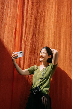 Young woman takes a selfie in front of a bright orange background