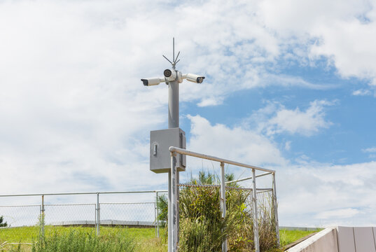 Outdoor security camera pole on green field under cloudy sky