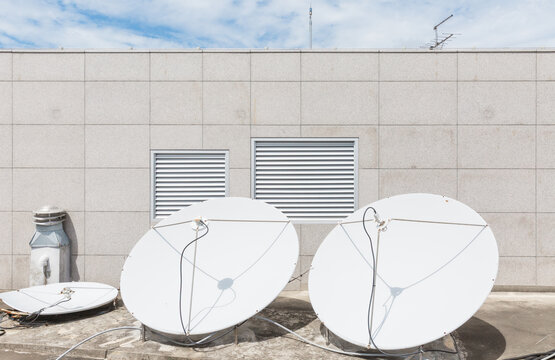 Two White Satellite Dishes on Building Rooftop under Blue Sky