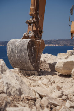 excavator on a cliff with sea at the background
