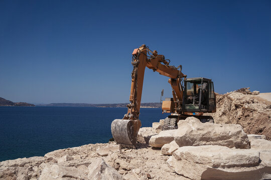 excavator on a cliff with sea at the background