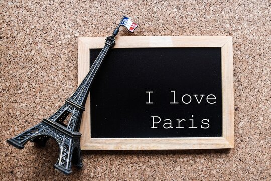 Sign that says I love Paris. Small black board on a cork board with a miniature Eiffel Tower and flag of France.