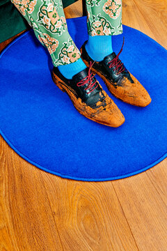 the muddy black shoes of a seated man on a round blue rug