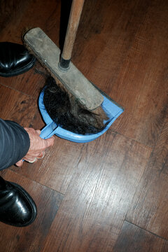 Hand holding a dustpan as broom sweeps hair clippings