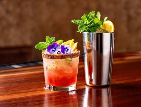 Cocktail with vibrant garnishes and colorful flowers captures attention. Mint leaves and lemon slices add freshness. Bar setting enhances enjoyment of this beverage