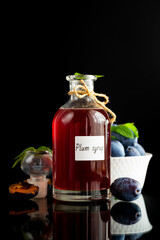 Homemade plum syrup with ripe fruit on black background © Peredniankina