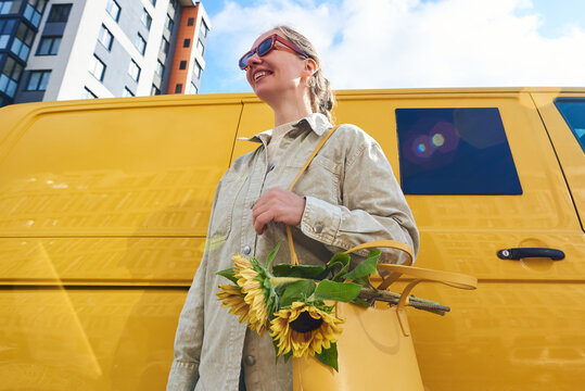 Woman smiles while holding sunflowers next to a yellow van