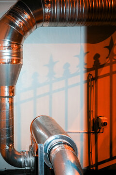 Industrial duct curves past ornate iron shadow on wall