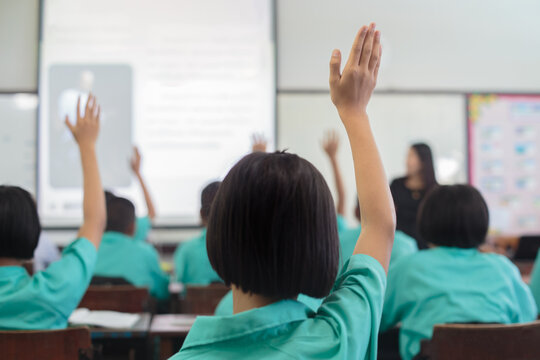 Rear View of Asian Students Raising Hands to Answer Question in Classroom