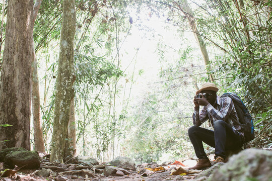 Side View of African Male Tourist Squatting and Taking Photos in Forest
