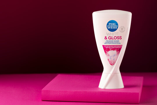 Perl Weiss White & Gloss whitening toothpaste standing upright on a pink display platform against a dark burgundy background. Studio product photograph with readable branding and generous copy space o