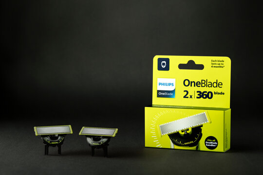 Two Philips OneBlade 360 replacement shaving heads displayed beside their lime-green retail packaging on a dark charcoal surface, with copy space. Studio still life illustrating electric grooming acce