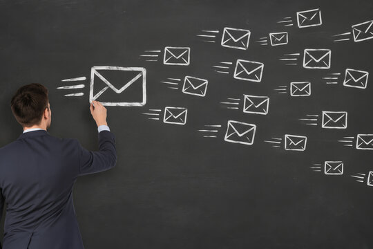 Businessman sketching flying email icons on chalkboard to illustrate mass email marketing, bulk messaging workflow, newsletter campaign and digital communication concept for business presentation