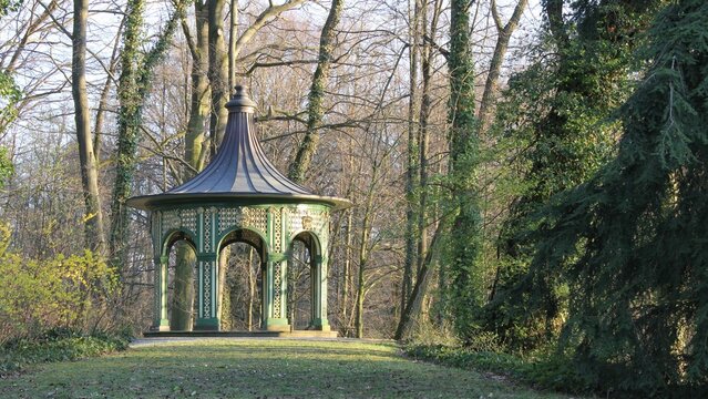 Ornate green and gold wooden gazebo in spring park forest