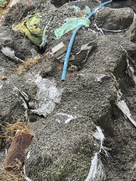 pile of construction waste dumped on the ground, hardened cement in torn sacks with blue plastic pipe and brick, environmental pollution and industrial dumping
