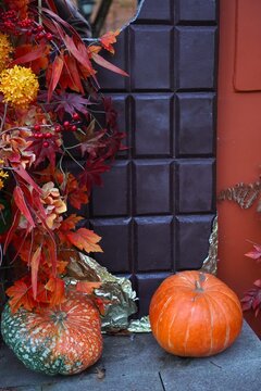 Autumn home decor near fireplace: pumpkins, red maple leaves, berries and gold ribbon. Seasonal preparation for Halloween and Thanksgiving celebration, fall holiday interior decoration.