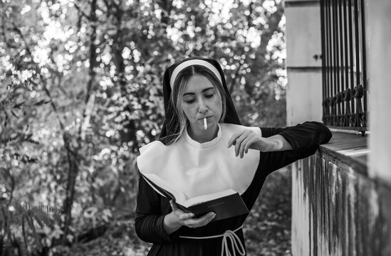Thoughtful woman wearing a traditional nun inspired habit and holding a cigarette. Dramatic conceptual portrait exploring faith, personal identity, inner conflict, rebellion and the contrast 