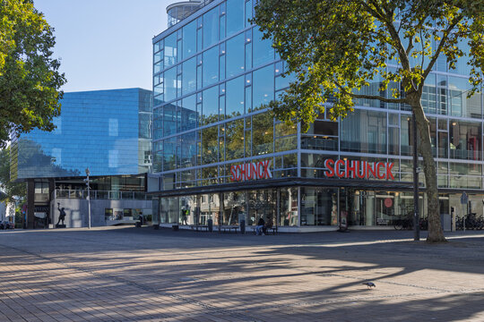Heerlen, Netherlands - 04 October 2026: Open urban plaza featuring the modern SCHUNCK Glaspaleis glass architecture with autumn trees casting long shadows on a sunny day.
