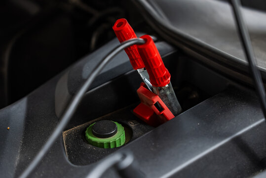 Jumper cables clamped securely onto the positive terminal of a vehicle battery compartment under the open hood, demonstrating maintenance and electrical charging inside an auto workshop.