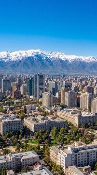 Aerial view of Santiago, Chile, showcasing its dense urban landscape with modern skyscrapers and traditional buildings, set against the majestic snow-capped Andes Mountains.