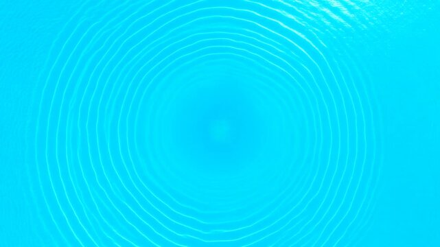 Concentric ripples emanate outward from a central point across a vibrant azure liquid surface, creating hypnotic circular wave patterns that suggest motion and a serene natural phenomenon