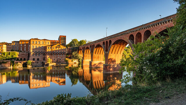 An morning view of the historic old town of Albi as the sun sets, featuring the Pont Neuf (New Bridge, also known as the Bridge of August 22, 1944), which spans the river Tarn.