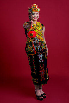 Young women in Kenyah Orang Ulu traditional clothing holding a red Chinese lantern on red background Chinese New Year Concept