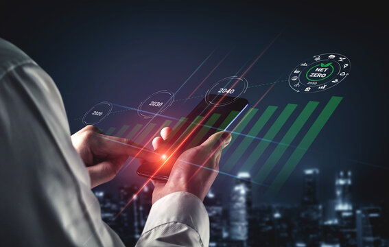 A business professional interacts with a smartphone displaying financial growth and sustainability data, set against a modern cityscape at night. Gantry