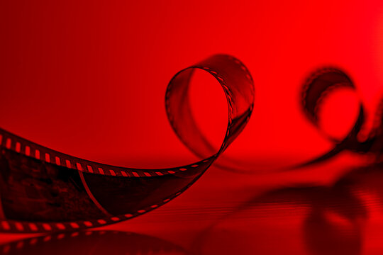 Curled 35mm film strip texture with red neon light background. Vintage cinema or photo film strip loops. Conceptual red backlighting for movie industry, analogue photography and darkroom concepts
