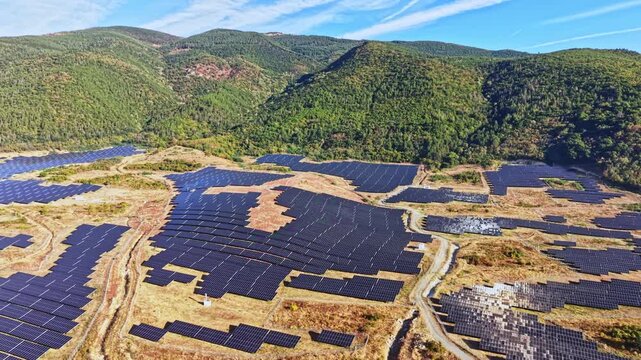 The scene shows a solar power farm set on hilly terrain with rows of solar panels arranged across the land under a blue sky.