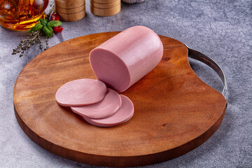 Wooden cutting board with pink bologna sausage and round slices, processed meat product © Andrei Starostin