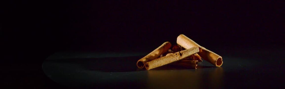 Cinnamon sticks rotating on black background, anamorphic close up