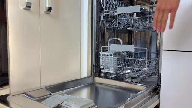 A person wipes the door of an empty dishwasher and closes it. Household cleaning, appliance maintenance and daily chores