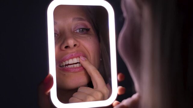 Young woman applies gel for sensitive teeth while looking in the mirror, showing dental care, oral treatment, and tooth sensitivity relief