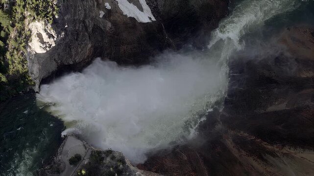 Aerial view of a powerful waterfall plunging into a rocky gorge with snow patches and forest