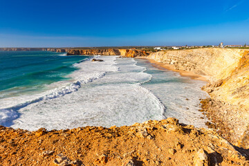 View of a picturesque beach on the Atlantic Ocean, with crashing waves under a blue sky, Sagres Viewpoint, Algarve region, Faro district, Portugal – background or wallpaper © anettastar