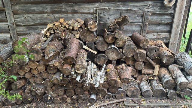 A neat pile of chopped firewood stacked against an old weathered log wall of a rustic wooden cabin, rural life, autumn preparation concept.