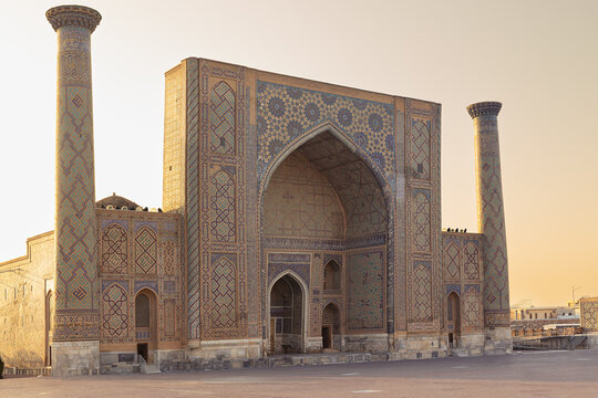 Ulugbek Madrasah facade at Registan Square in Samarkand bathed in golden evening light. Intricate geometric tilework and twin minarets frame the grand iwan portal. Ideal for travel publications.