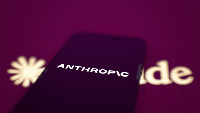 The Anthropic logo displayed on a smartphone, with a projected Claude logo. Anthropic commits $100 million to train 10,000 AI engineers by 2027. October 4, 2026, Lisbon, Portugal.