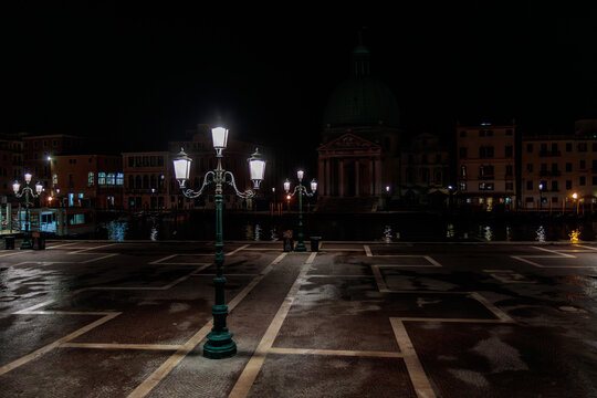 Empty square outside Santa Lucia railway station before dawn with street lamps lit and San Simeon Piccolo church in Venice