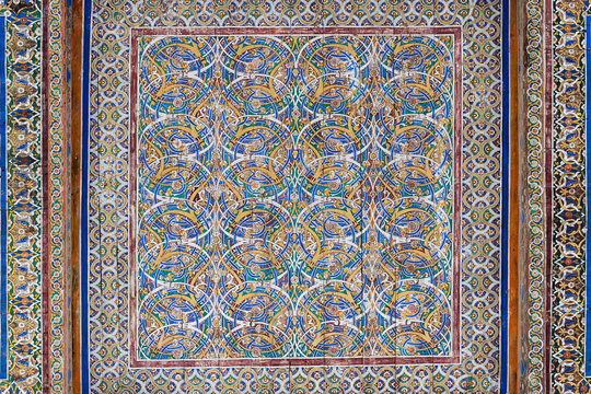 Ornate painted ceiling panel with intricate arabesque patterns at Muhammad Rahim Khan Madrasah in Khiva. Traditional Uzbek decorative art featuring blue, gold, and green interlocking floral motifs.