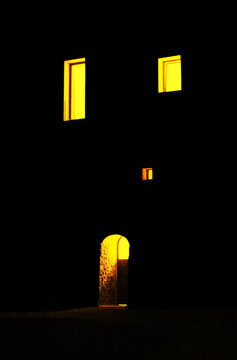 The facade of a building, door and windows with a yellow light on a black background. Book cover, graphic, illustration, poster
