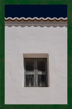 An old wooden window on a white facade with a wavy gutter inside a vintage green frame
