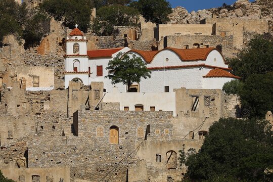 White church with red tile roofs surrounded by ancient stone ruins and rocky backdrop, Lost Place, Abandoned Village, Mikro Chorio, Church of the Assumption of Mary, Zero Waste Island, Tilos, Dodecanese, Greek Islands, Greece