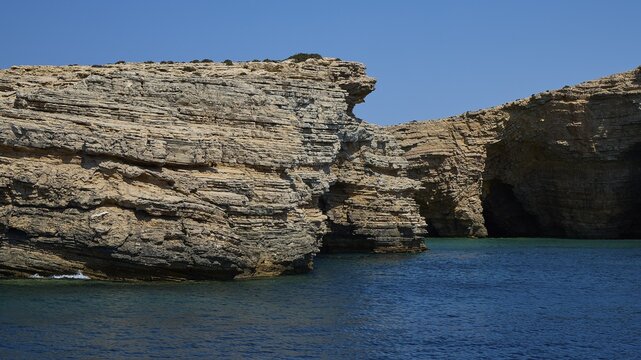 Caves by the sea, cliffs with striking rock formations and deep blue water under a clear sky, Makronisi Kasou, Lipsi, Dodecanese, Greek Islands, Greece