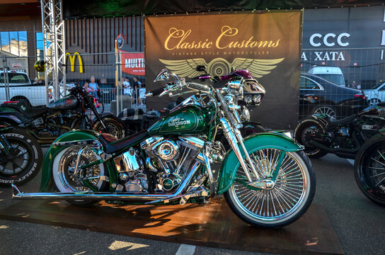 Custom green Harley-Davidson Softail lowrider featuring chrome spoked wheels, fishtail exhausts, and whitewall tires, showcasing Chicano bike culture